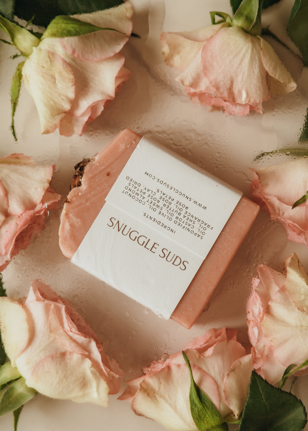 Bar of soap labeled 'Snuggle Suds' surrounded by pink roses on a light background