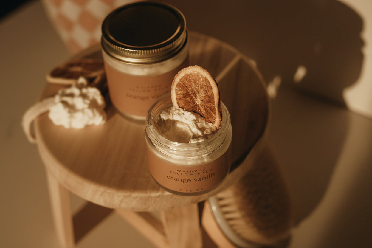 Jar of orange vanilla candle with a dried orange slice on top, placed on a wooden surface.